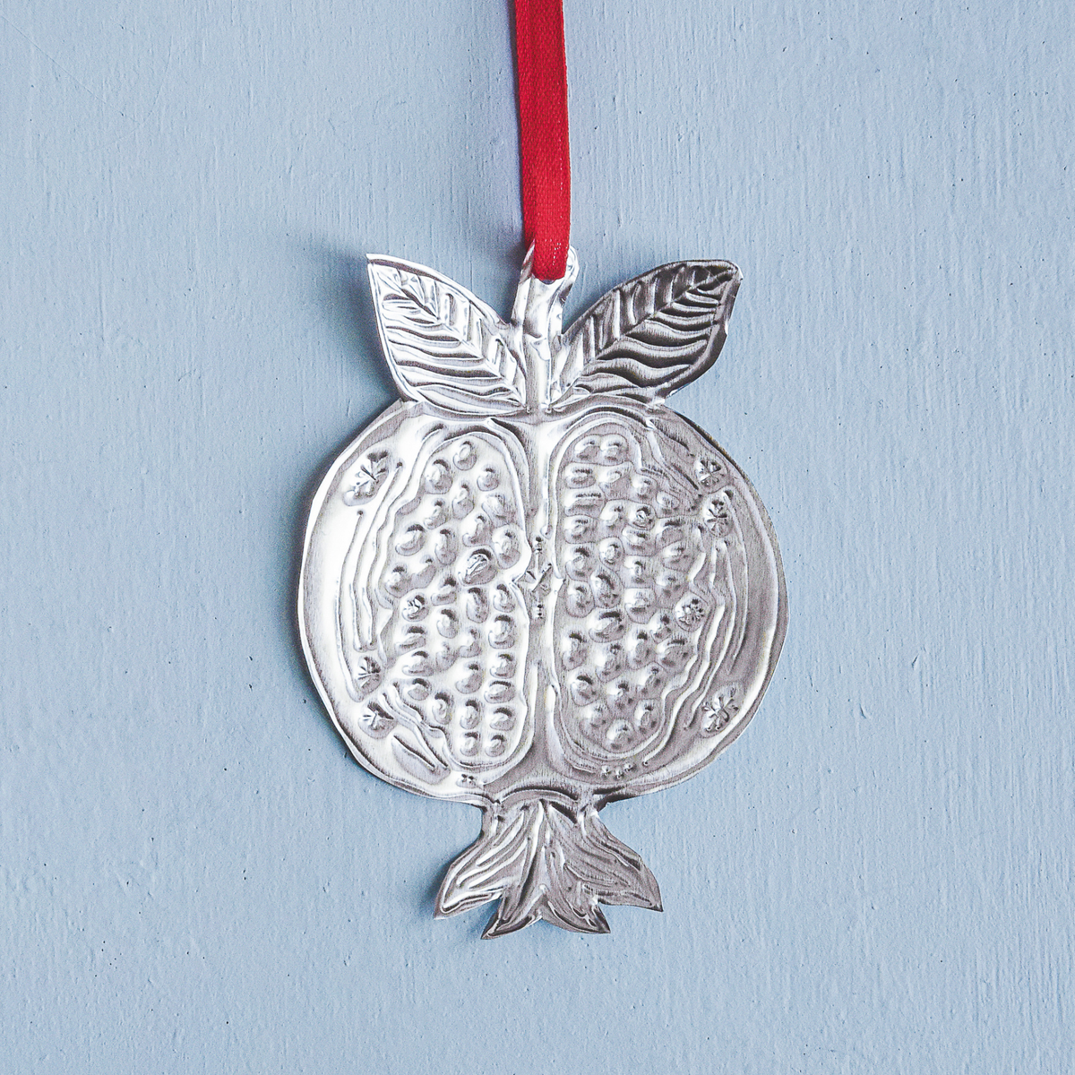 Silver pomegranate ornament with a red ribbon on a light blue background