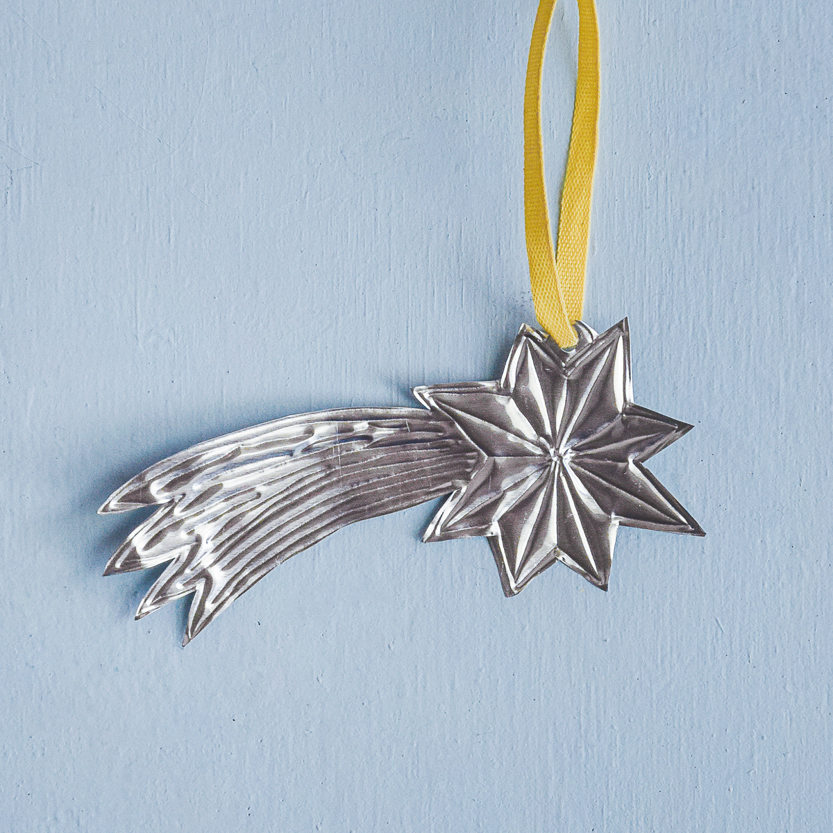 Silver star-shaped ornament on a yellow ribbon against a light blue background