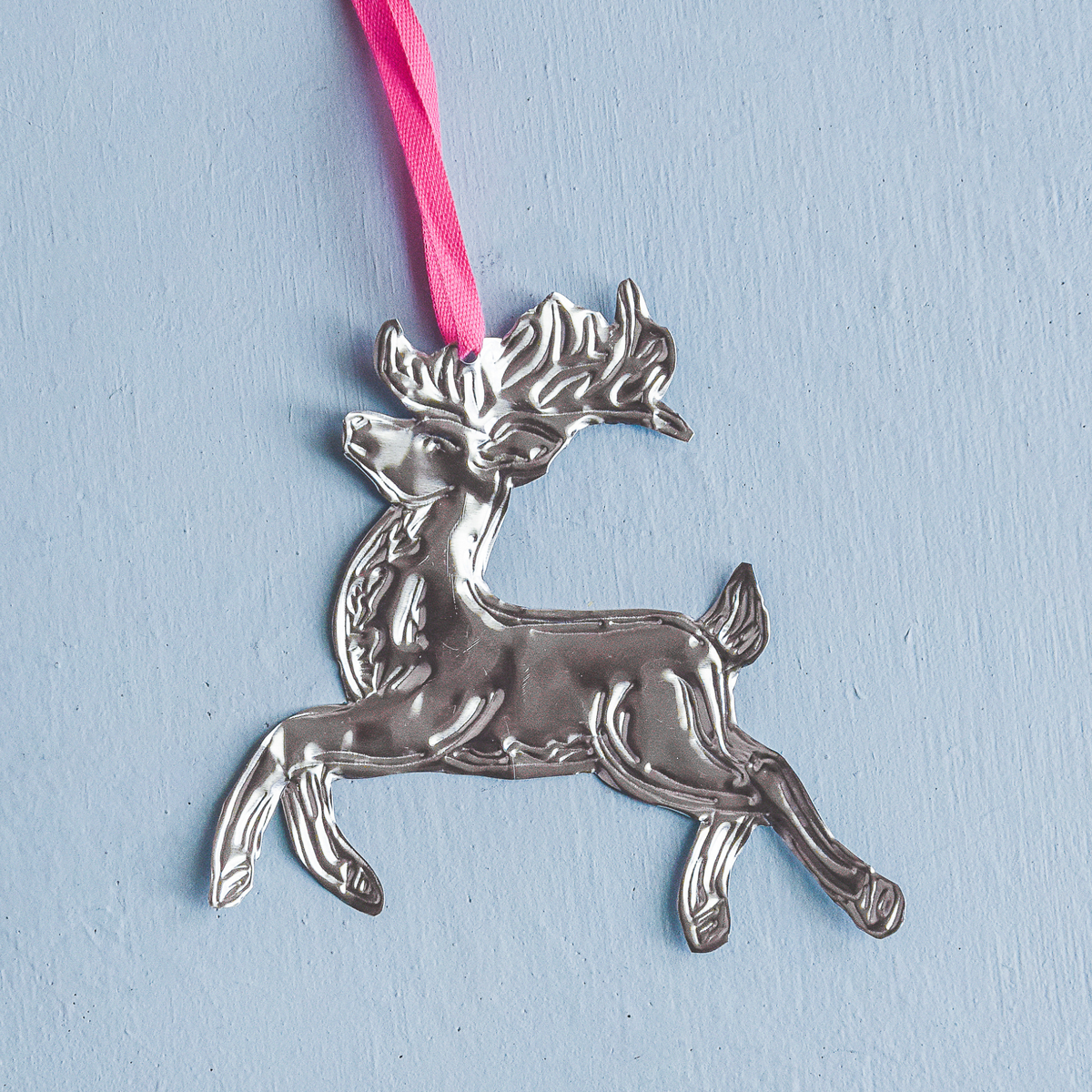 Silver reindeer ornament with a pink ribbon on a light blue background