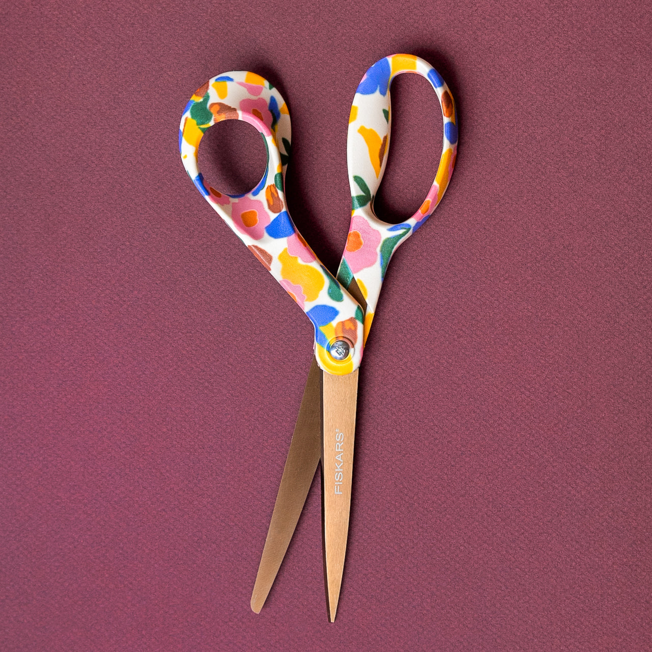 Scissors handle has playful abstract floral elements that are blue, yellow, green and pink. The blade is a bronze titanium finish.