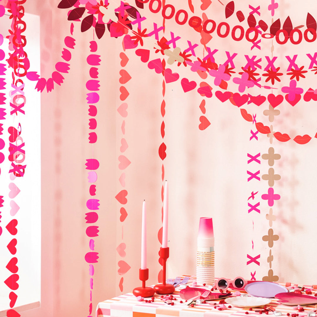 Tablescape scene for Valentine&#39;s Day. Long garlands made of paper symbols that celebrate love. Bright pinks and reds. 