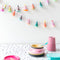 Mini party hat garland strung on twine on a wall with party supplies on the table.